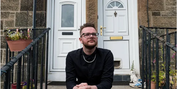 White man sitting on steps outside house looking pensive